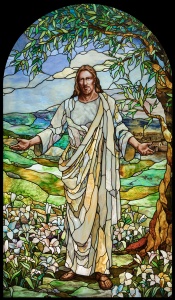 stained glass of christ with arms extended next to a tree