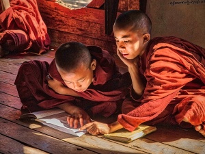 two young boys in the traditional attire of tibetan buddhist monks sit next to each other reading a book