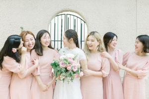 A bride with 6 bridesmaids, the bride wearing a white dress and holding a pink bouquet, and the bridesmaids all in half-sleeved pink dresses