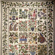A quilt with a beige background and a floral leaf motif throughout
