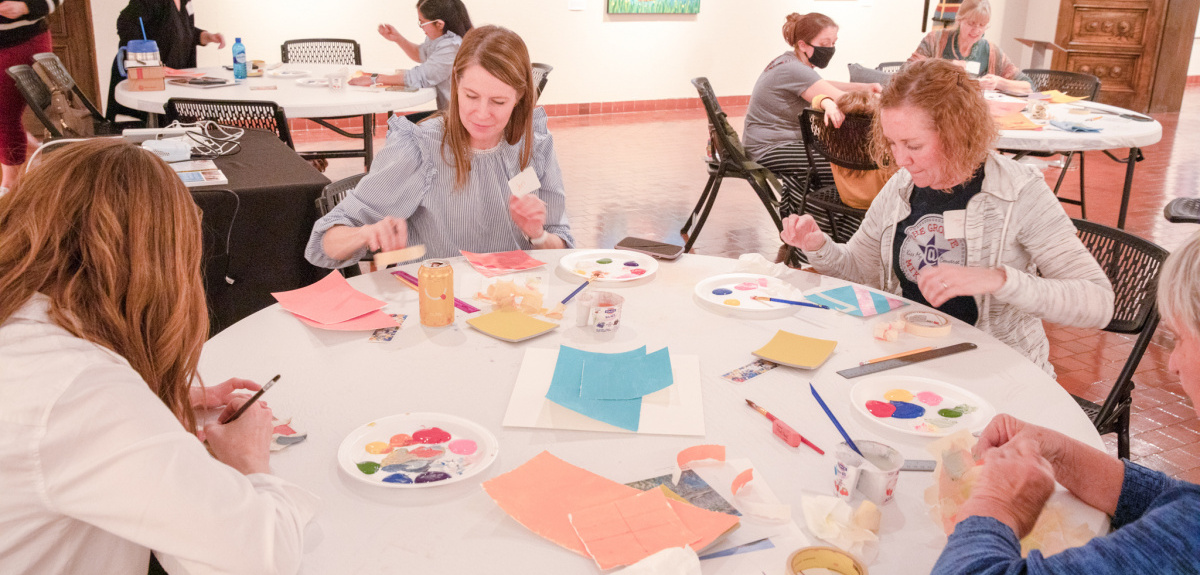 Group of white women at round table painting with bright colors.